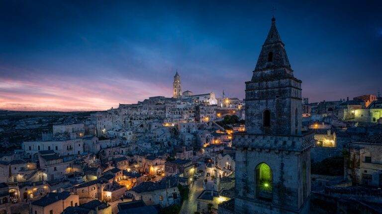 Vista notturna di Matera con case scavate nella roccia illuminate, simili a un presepe incantevole.