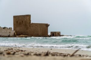 Spiaggia di Capo Rizzuto con sabbia rossa e castello aragonese affacciato sul mare.