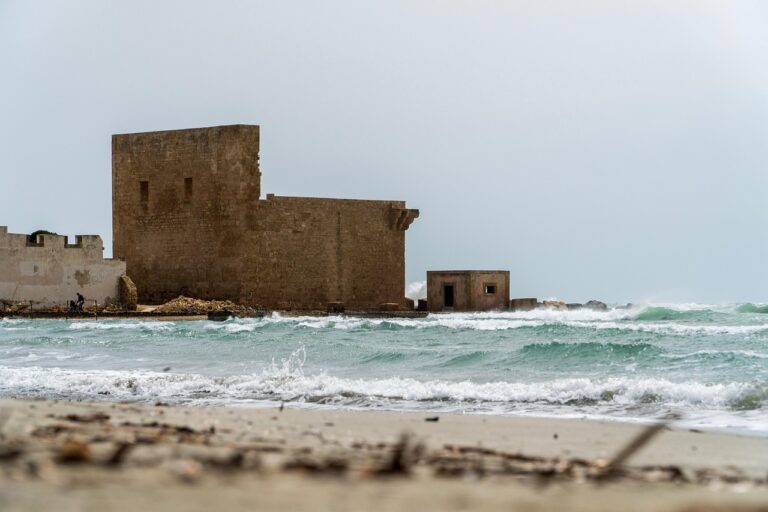 Spiaggia di Capo Rizzuto con sabbia rossa e castello aragonese affacciato sul mare.